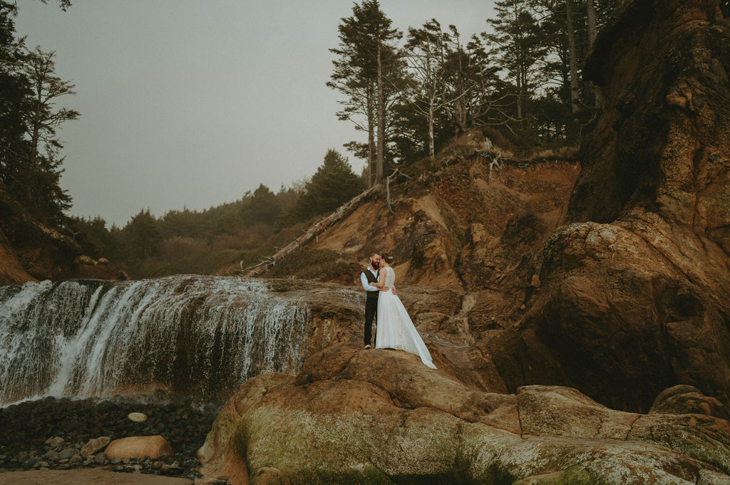 newly eloped couple at hug point oregon beach for elopement with waterfall backdrop