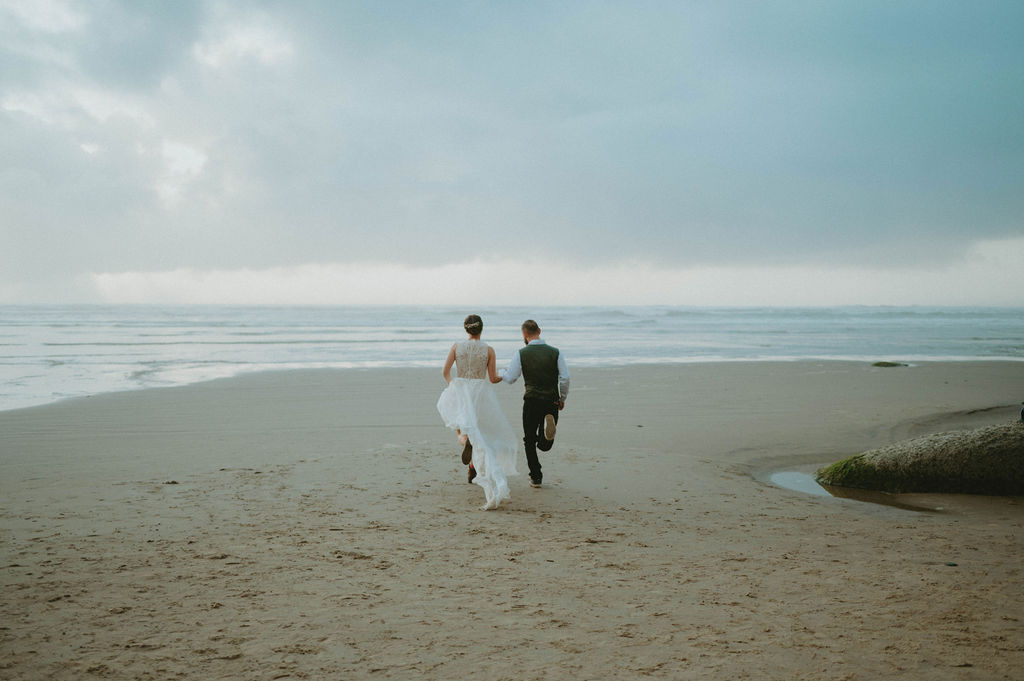 newly eloped couple holding hands running on oregon coast beach