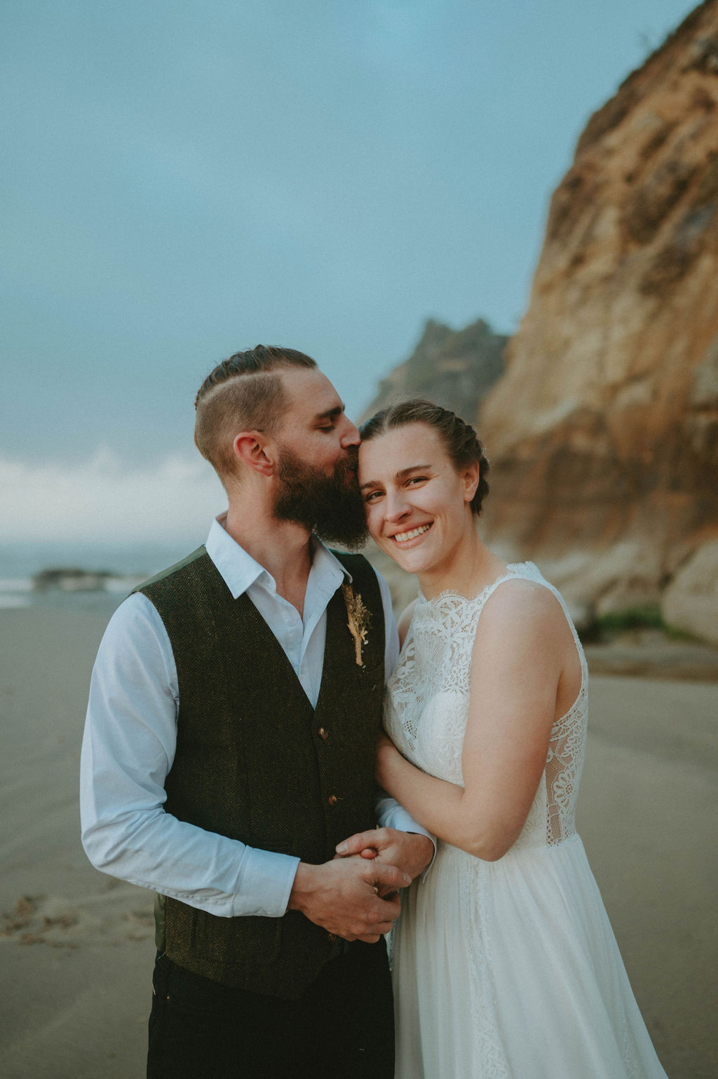 husband kissing wife on forehead during beach elopement